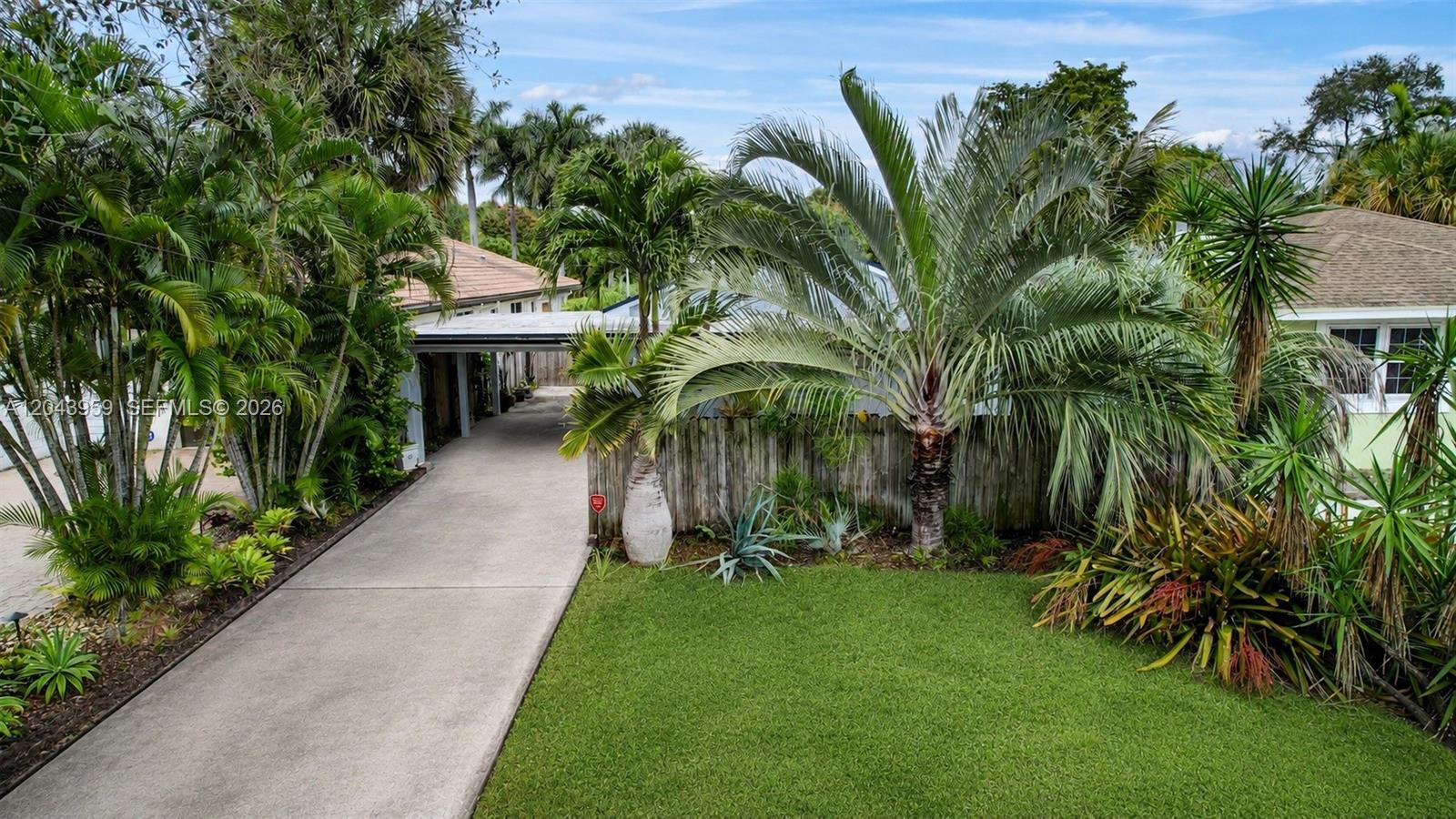 A concrete driveway leads to a covered carport beside a house with lush tropical landscaping — 1401 NE 33rd St, Oakland Park FL 33334, OAKLAND PARK, FL