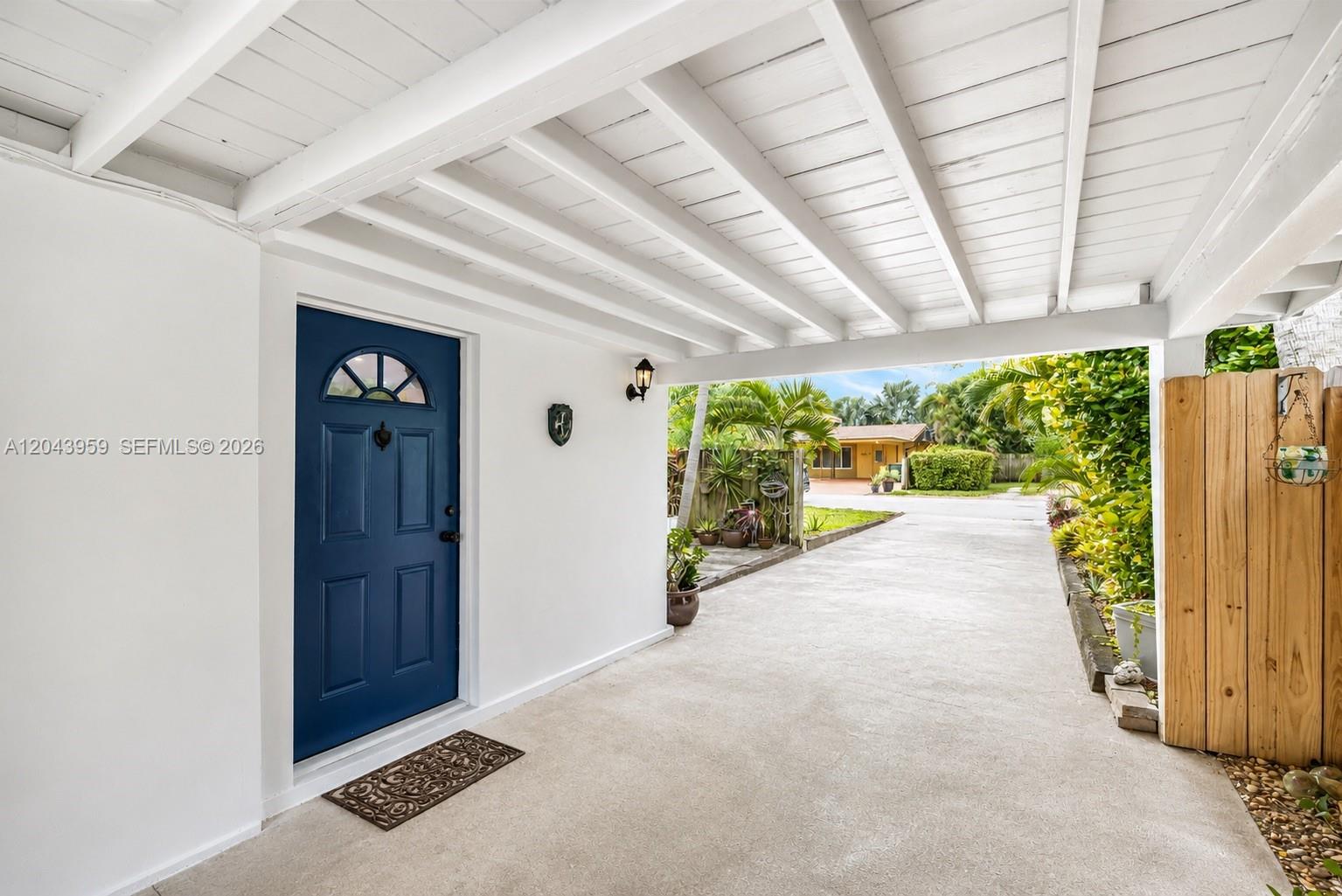 A blue front door opens onto a concrete driveway under a white wooden carport — 1401 NE 33rd St, Oakland Park FL 33334, OAKLAND PARK, FL