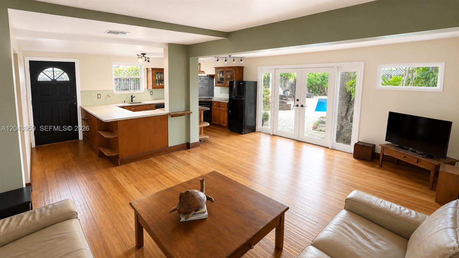 A living room with hardwood floors connects to a kitchen featuring wood cabinetry and appliances — 1401 NE 33rd St, Oakland Park FL 33334, OAKLAND PARK, FL