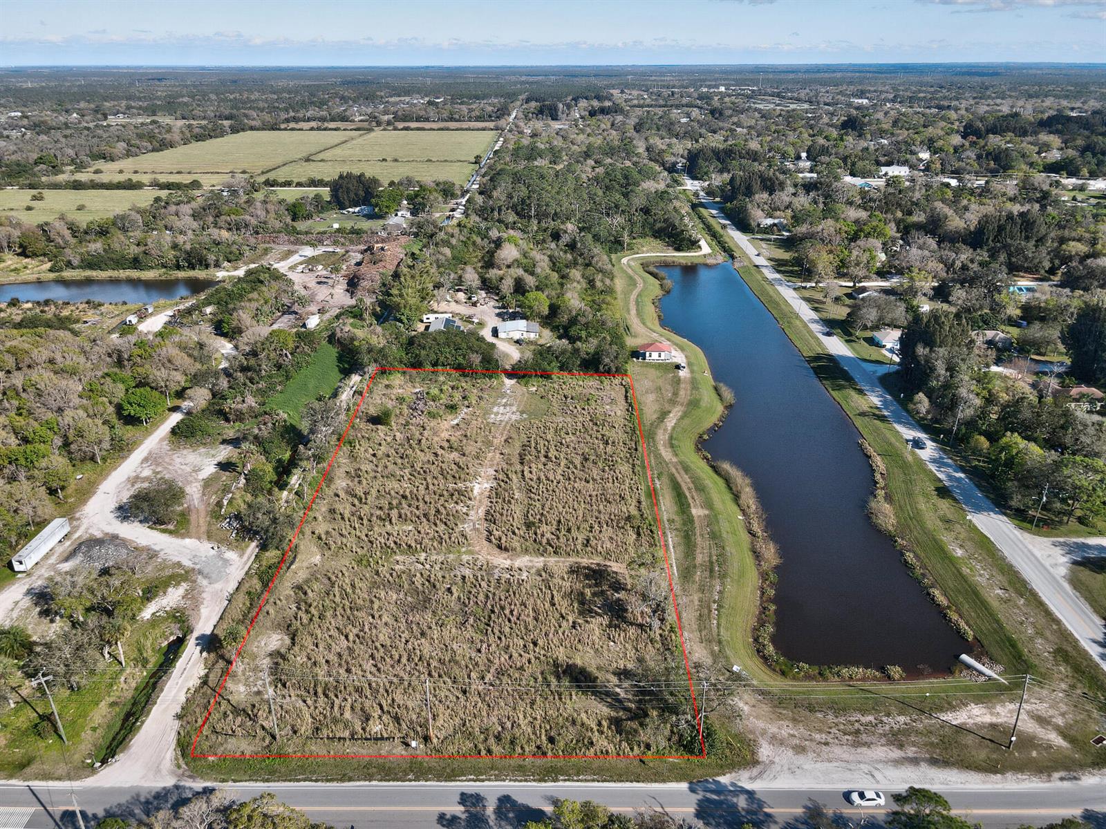 An aerial view shows a rectangular, grass-covered vacant lot bordered by a road and pond — 13765 99th Street, Fellsmere FL 32948, FELLSMERE, FL