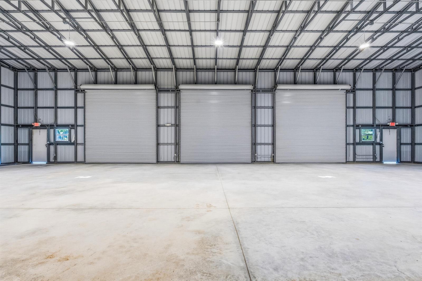 A large, empty industrial warehouse space features concrete floors, metal walls, and three roll-up doors — VERO BEACH, FL