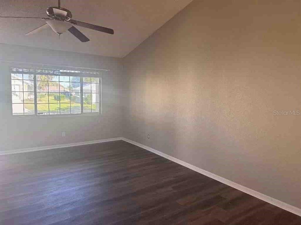An empty room features dark wood-look flooring, light gray walls, and a ceiling fan — 5110 NW 19TH PLACE, OCALA, FL
