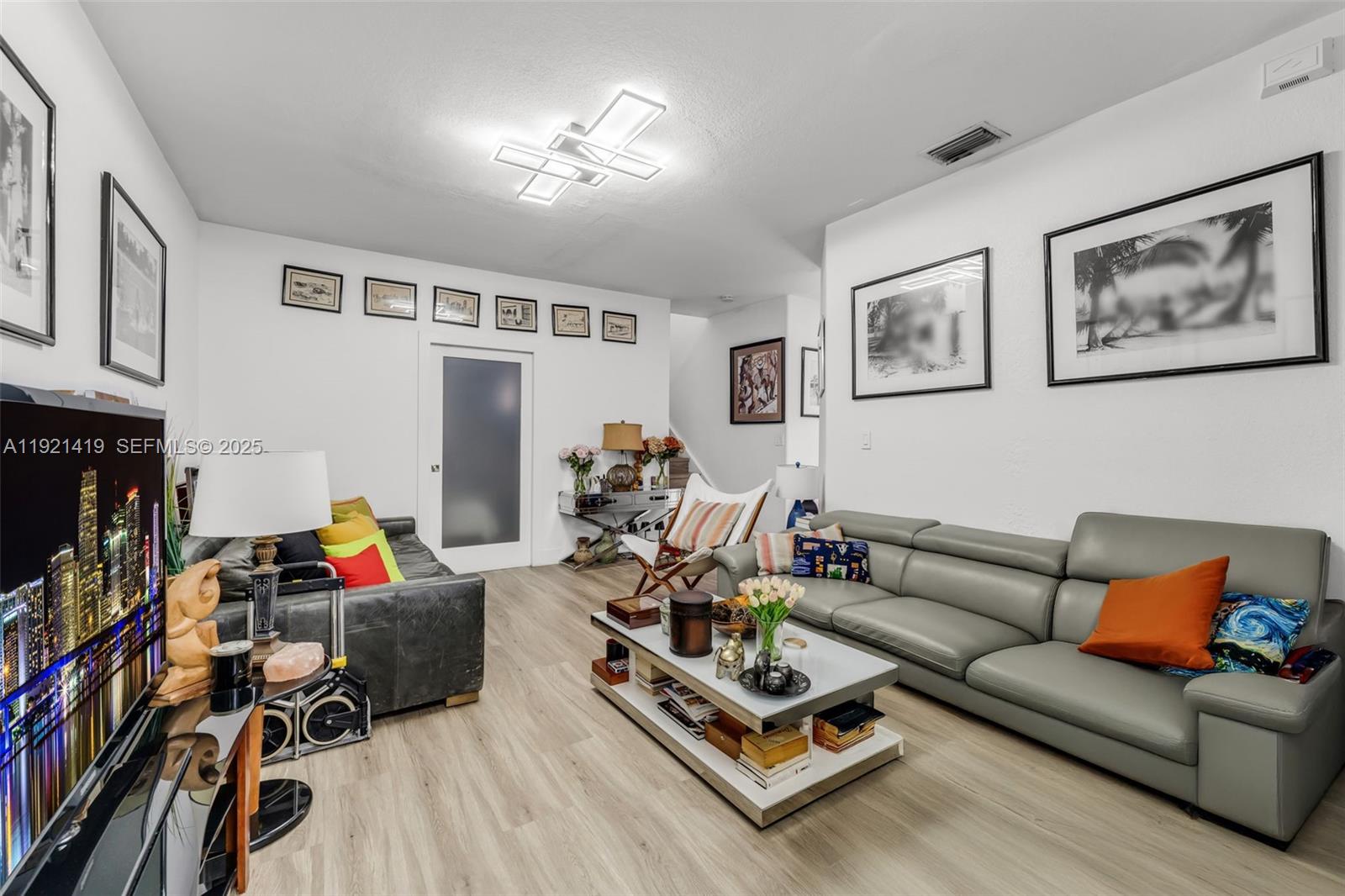 A living room features light wood flooring, a grey leather sofa, and a modern ceiling light — 5610 NW 107th Ave # 1306, Doral FL 33178, DORAL, FL