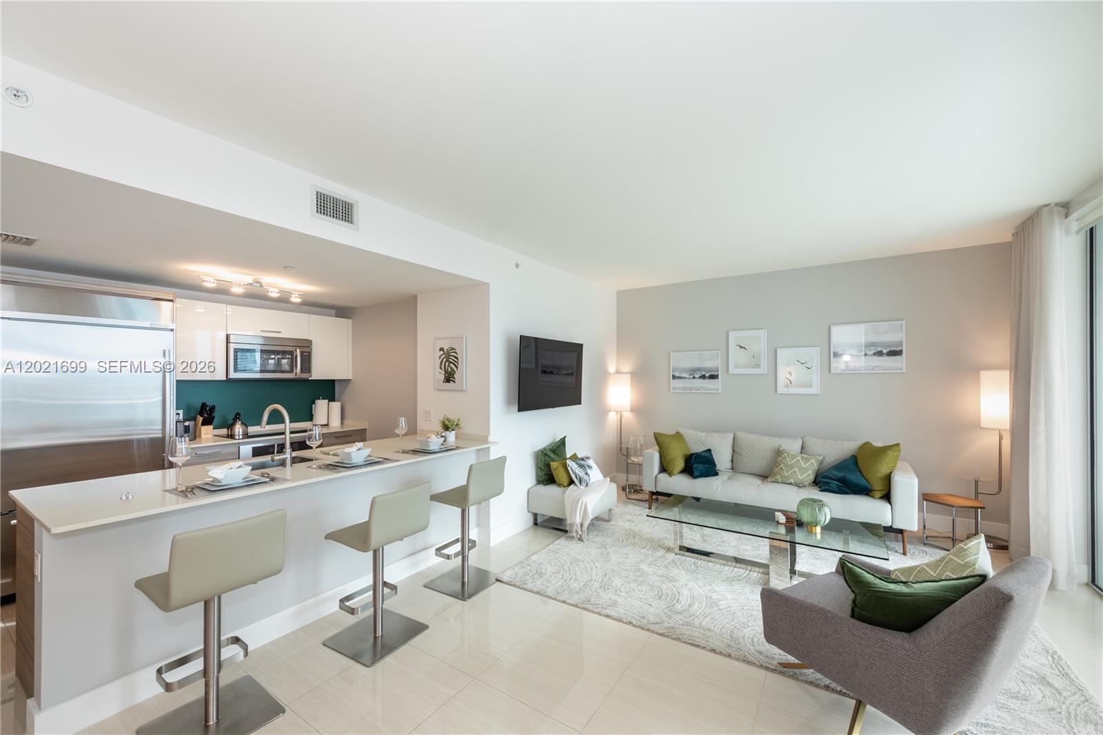 A modern open-concept living room and kitchen feature a breakfast bar and neutral decor — 1300 Brickell Bay Dr # 2900, Miami FL 33131, MIAMI, FL