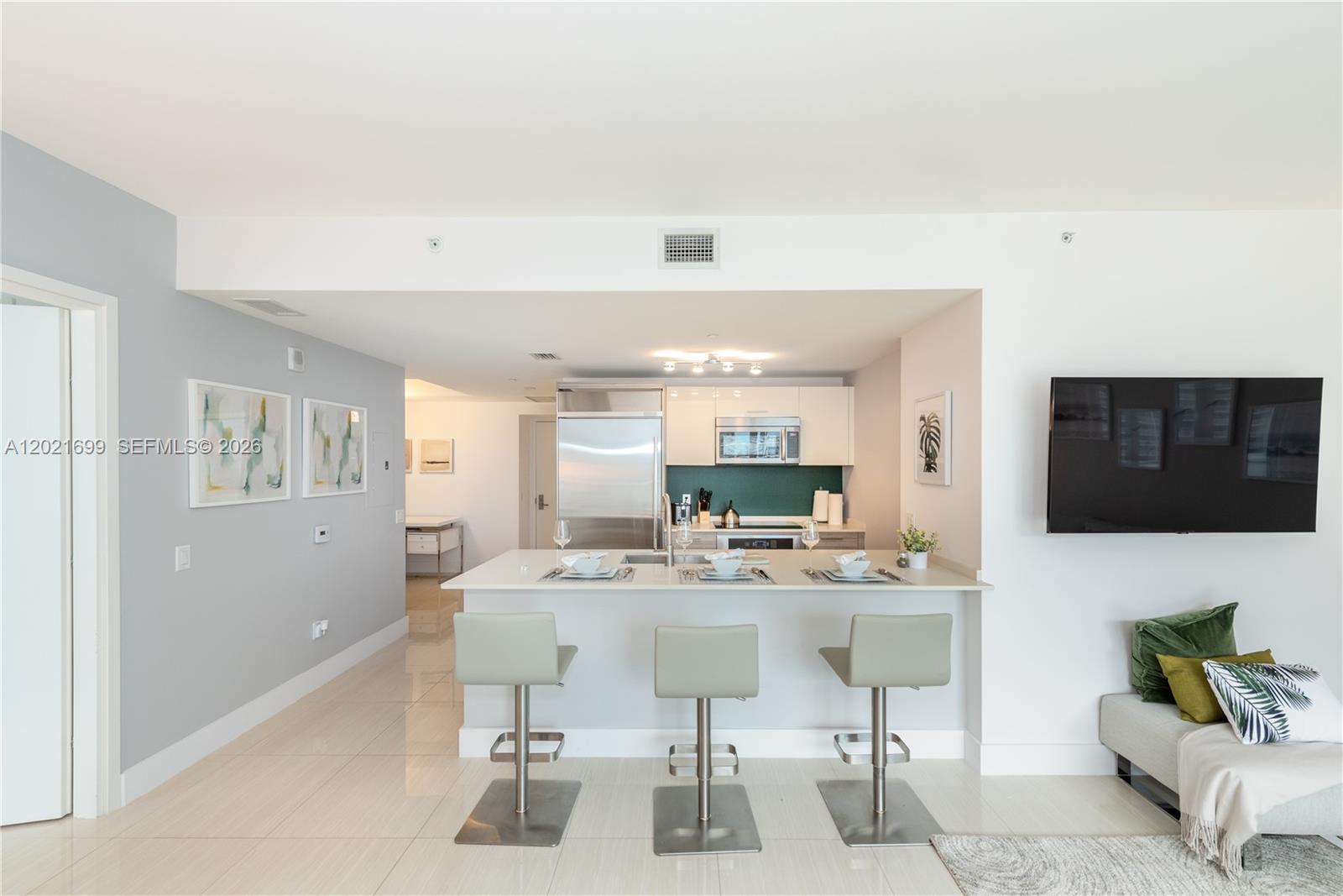 A modern kitchen features a breakfast bar with three stools and stainless steel appliances — 1300 Brickell Bay Dr # 2900, Miami FL 33131, MIAMI, FL