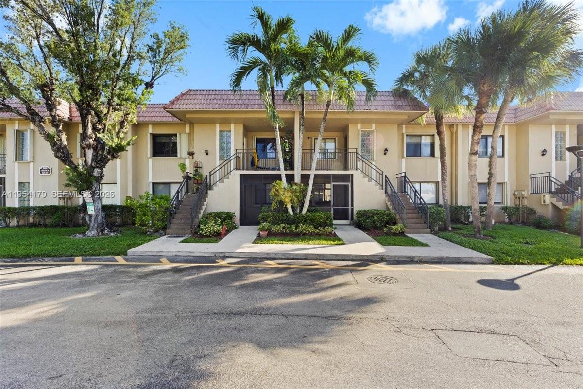A two-story tan apartment building features exterior staircases, palm trees, and a paved parking lot — 302 Lakeview Dr # 203, Weston FL 33326, WESTON, FL