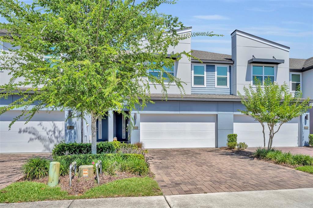 A multi-story townhouse exterior with a paved driveway, two-car garage, and a small front garden — 1351 MERRYDALE WAY, WINTER PARK, FL