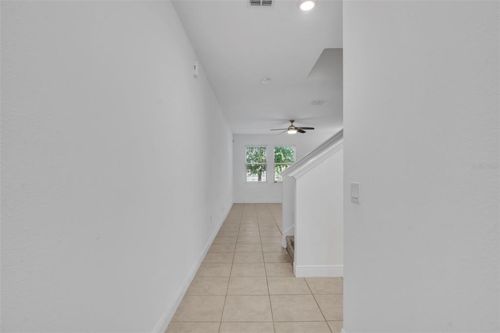 A narrow hallway with light-colored tile flooring leads toward a room with windows — 1351 MERRYDALE WAY, WINTER PARK, FL