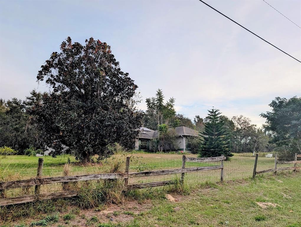 A house sits behind a wooden fence and a large tree in a grassy yard — 310 TOMATO HILL ROAD, LEESBURG, FL