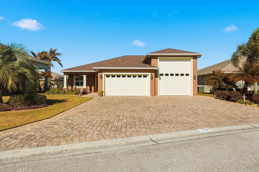A single-story house with a two-car garage and a paved driveway under a blue sky — 719 TEABERRY TRAIL, POLK CITY, FL