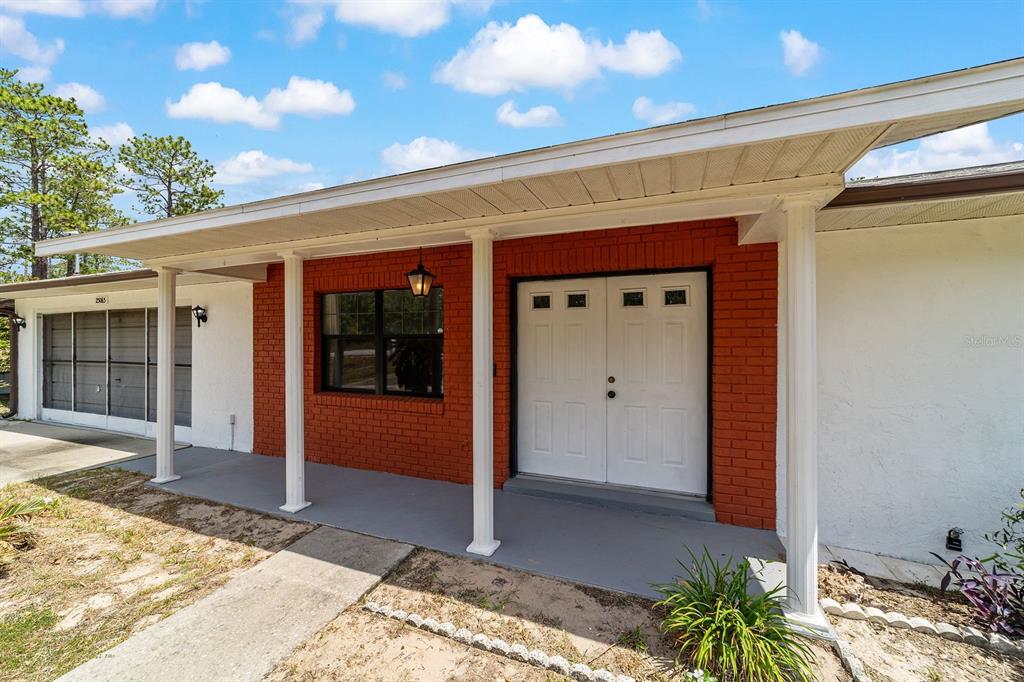 The exterior of a house features a red brick facade, white double doors, and columns — 23063 SW EDGEWATER BOULEVARD, DUNNELLON, FL