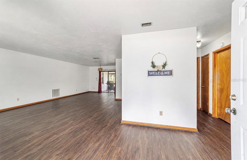 An empty living area features dark wood-look flooring, white walls, and a welcome sign — 23063 SW EDGEWATER BOULEVARD, DUNNELLON, FL