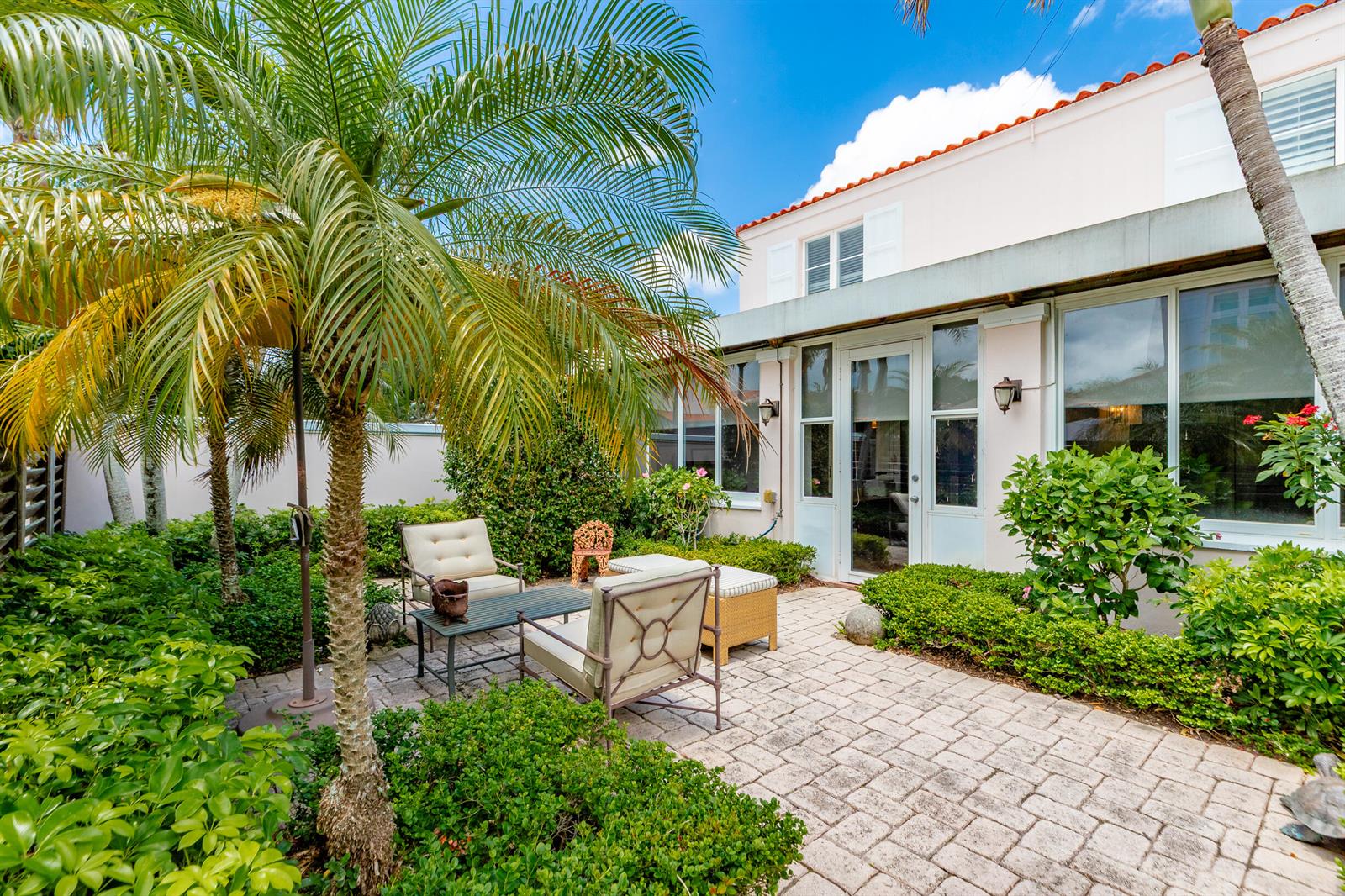 A paved patio with outdoor furniture sits beside a house with large windows and palm trees — VERO BEACH, FL