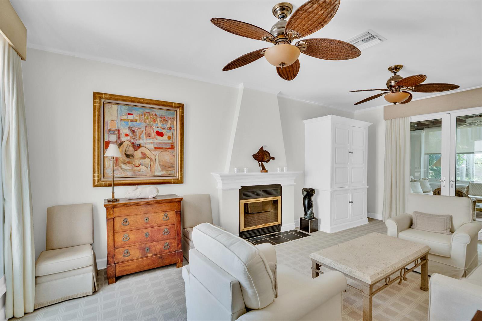 A living room features a fireplace, two ceiling fans, white armchairs, and a wooden chest — VERO BEACH, FL
