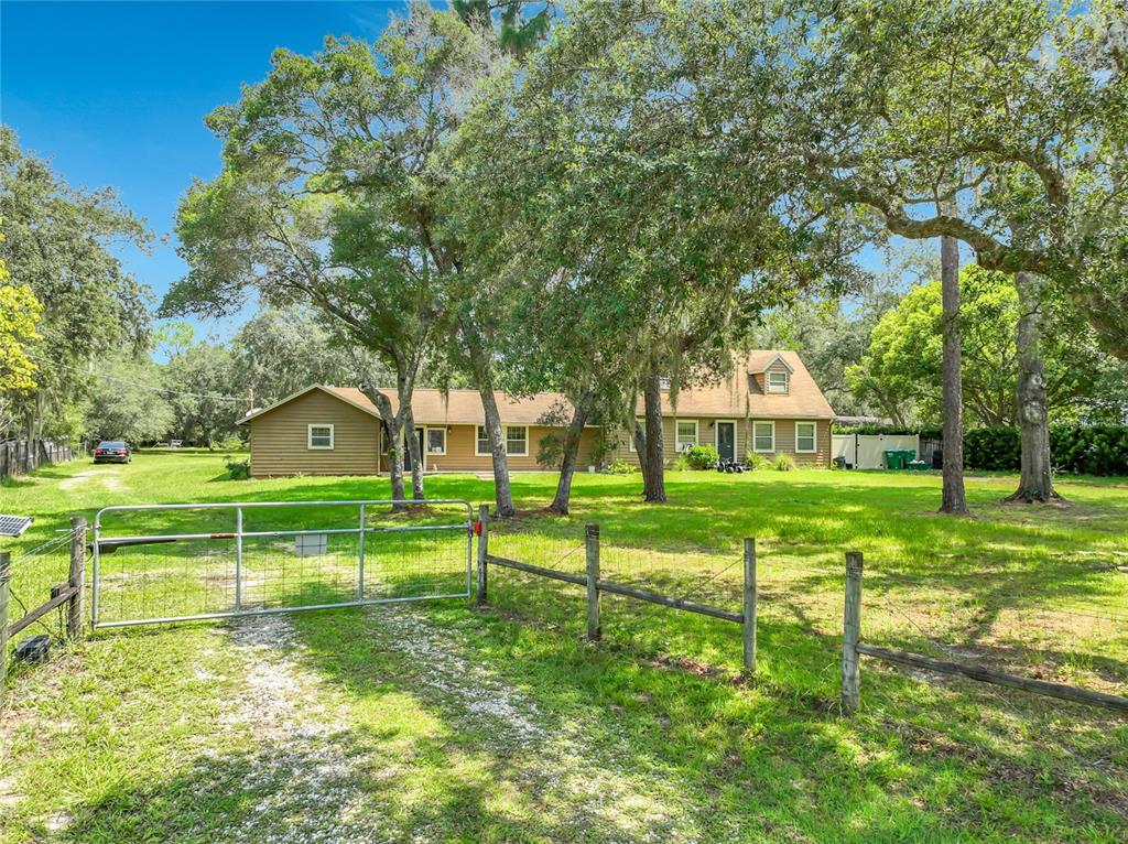 A tan, single-story house with a gabled roof sits behind a metal gate and fence — 670 E STATE ROAD 46, GENEVA, FL