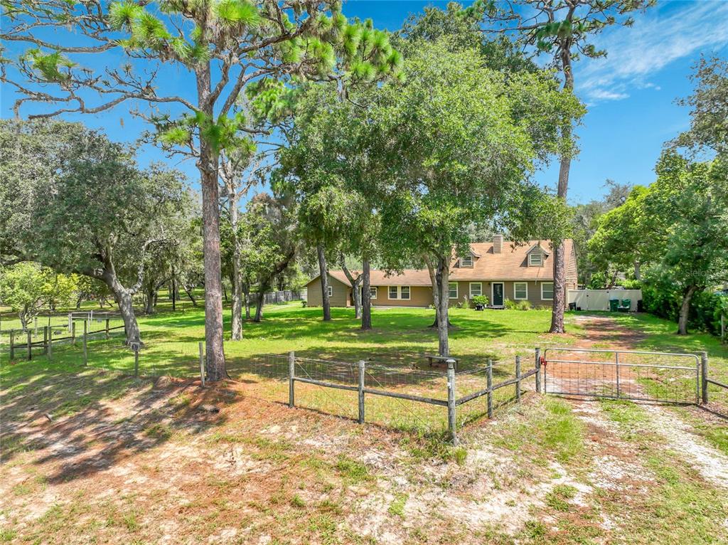 A single-story house with a brown exterior sits on a grassy lot with many trees — 670 E STATE ROAD 46, GENEVA, FL
