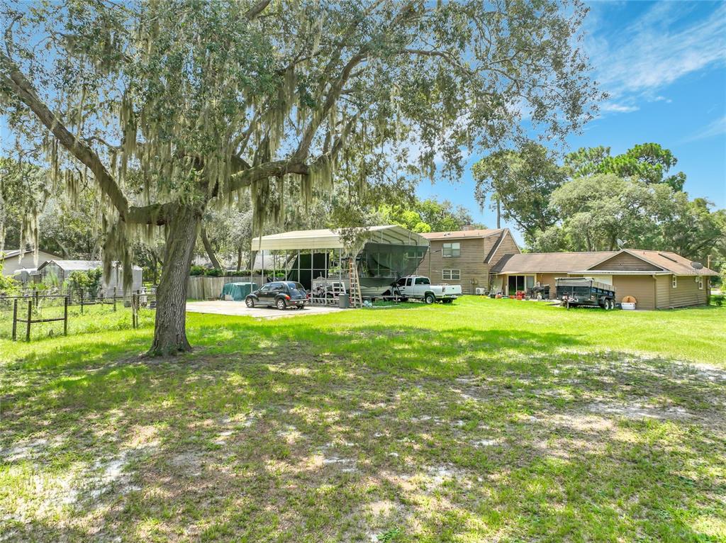A large backyard features a mature tree, a metal carport, and a brown house — 670 E STATE ROAD 46, GENEVA, FL