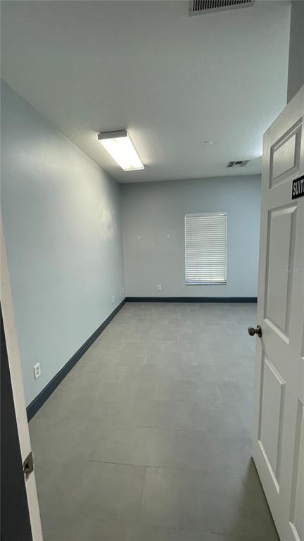 An empty office room features light blue walls, gray tile flooring, and a single window — 722 PATRICK STREET UNIT 208, KISSIMMEE, FL