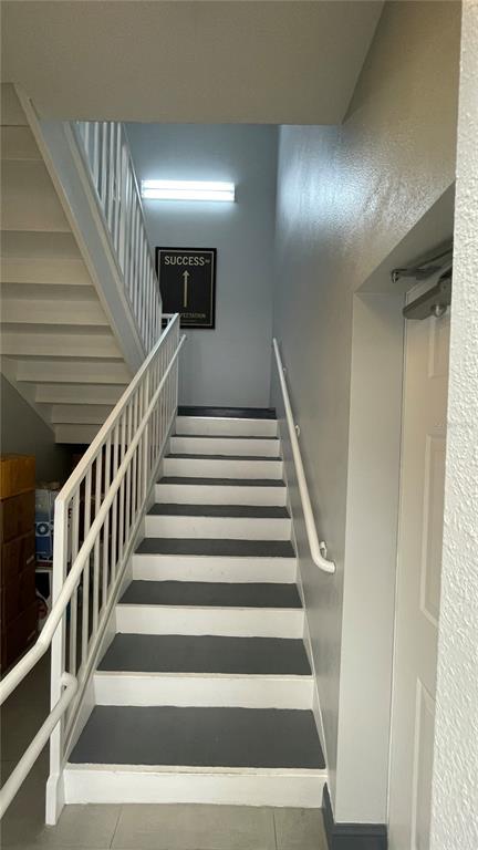An indoor staircase with white railings and gray-painted treads leads to an upper landing — 722 PATRICK STREET UNIT 208, KISSIMMEE, FL