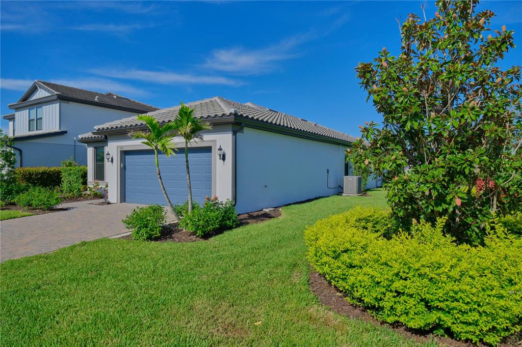 A single-story house with a blue garage door, a paved driveway, and a large front bush — 818 PINTAIL COVE, BRADENTON, FL