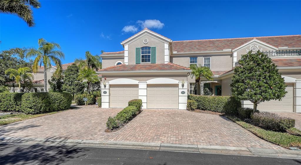 A two-story townhouse features a paved driveway, two garage doors, and surrounding landscaping — 5235 PARISIENNE PLACE UNIT 101B28, SARASOTA, FL