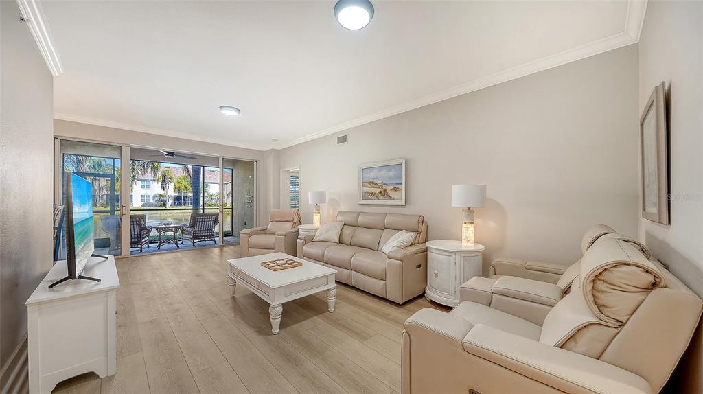 A living room with light wood floors, beige leather furniture, and a sliding door to a patio — 5235 PARISIENNE PLACE UNIT 101B28, SARASOTA, FL