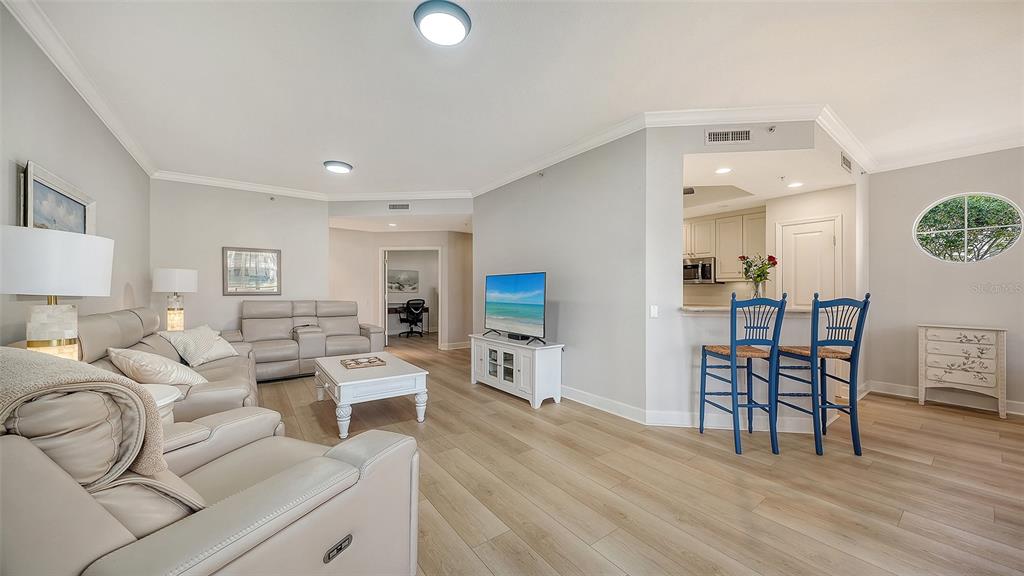 A living room with light wood floors, a beige sofa, and a kitchen breakfast bar — 5235 PARISIENNE PLACE UNIT 101B28, SARASOTA, FL