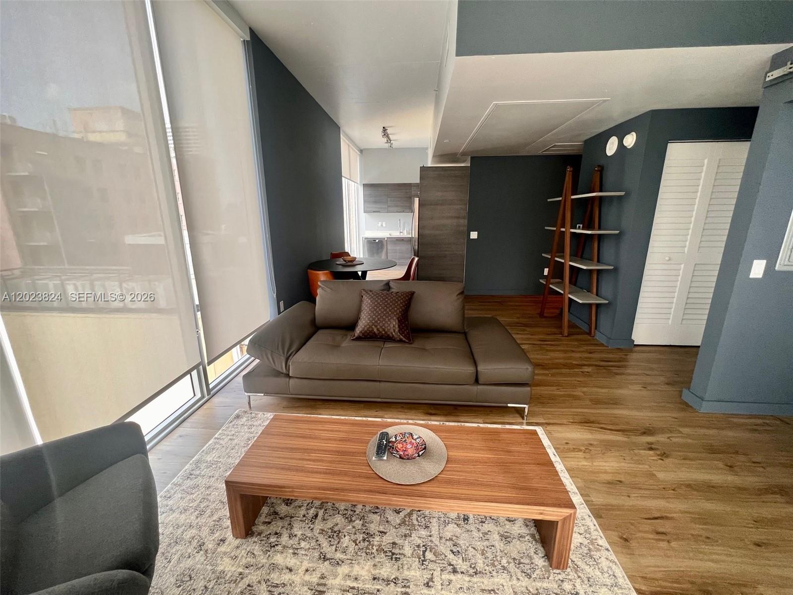 A living room features a brown leather sofa, wood coffee table, and dark blue walls — 151 SE 1st St # 810, Miami FL 33131, MIAMI, FL