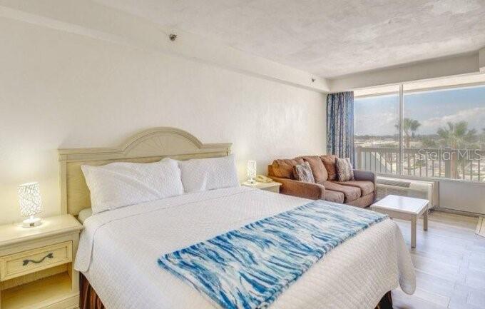 A bedroom features a bed with a blue patterned runner, a sofa, and a balcony — 2700 N ATLANTIC AVENUE UNIT 421, DAYTONA BEACH, FL