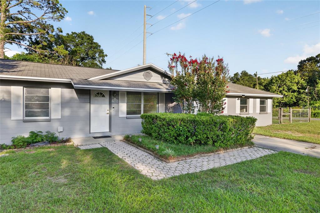 A single-story gray house with a white door, a paved walkway, and a large hedge — 17409 NW 240TH TERRACE, HIGH SPRINGS, FL