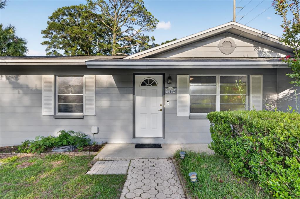 A gray, single-story house features a white front door, shuttered windows, and a paved walkway — 17409 NW 240TH TERRACE, HIGH SPRINGS, FL