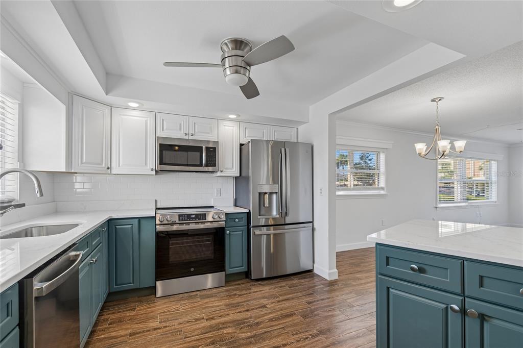 A kitchen with white upper cabinets, blue lower cabinets, stainless steel appliances, and wood-look flooring — 4575 COVE CIRCLE UNIT 101, ST PETERSBURG, FL
