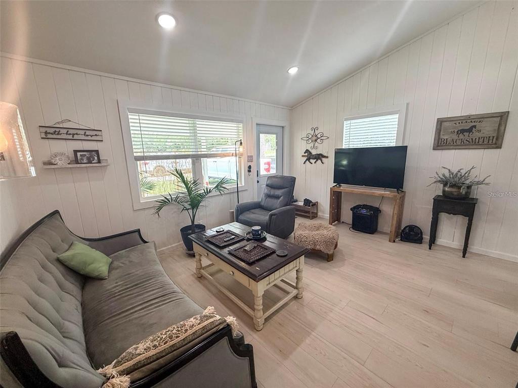 A living room features white paneled walls, light wood-look flooring, a sofa, and a television — 11770 N ANGUS HILLS TERRACE, DUNNELLON, FL