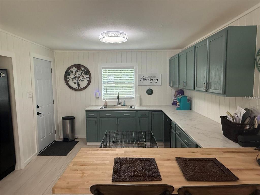 A kitchen features teal cabinets, white countertops, wood-topped island seating, and white paneled walls — 11770 N ANGUS HILLS TERRACE, DUNNELLON, FL