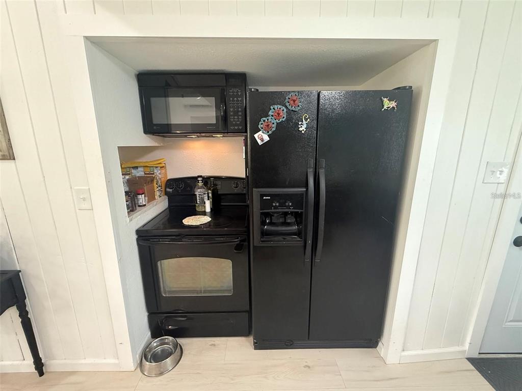 A kitchen features a black stove, microwave, and side-by-side refrigerator recessed into a wall alcove — 11770 N ANGUS HILLS TERRACE, DUNNELLON, FL