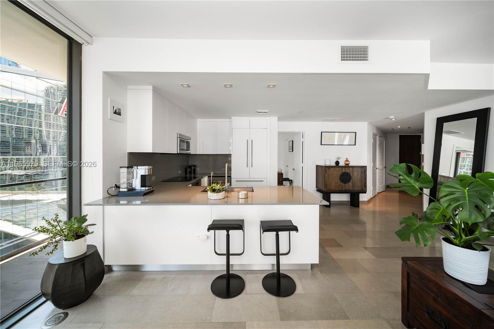 A modern kitchen with white cabinets and quartz countertops overlooks a living area and balcony — 68 SE 6th St # 1201, Miami FL 33131, MIAMI, FL