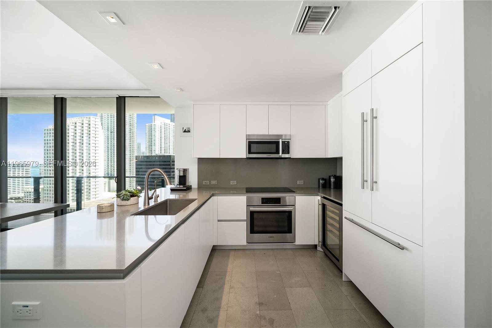 A modern kitchen features white cabinetry, a gray island with two stools, and tile flooring — 68 SE 6th St # 1201, Miami FL 33131, MIAMI, FL