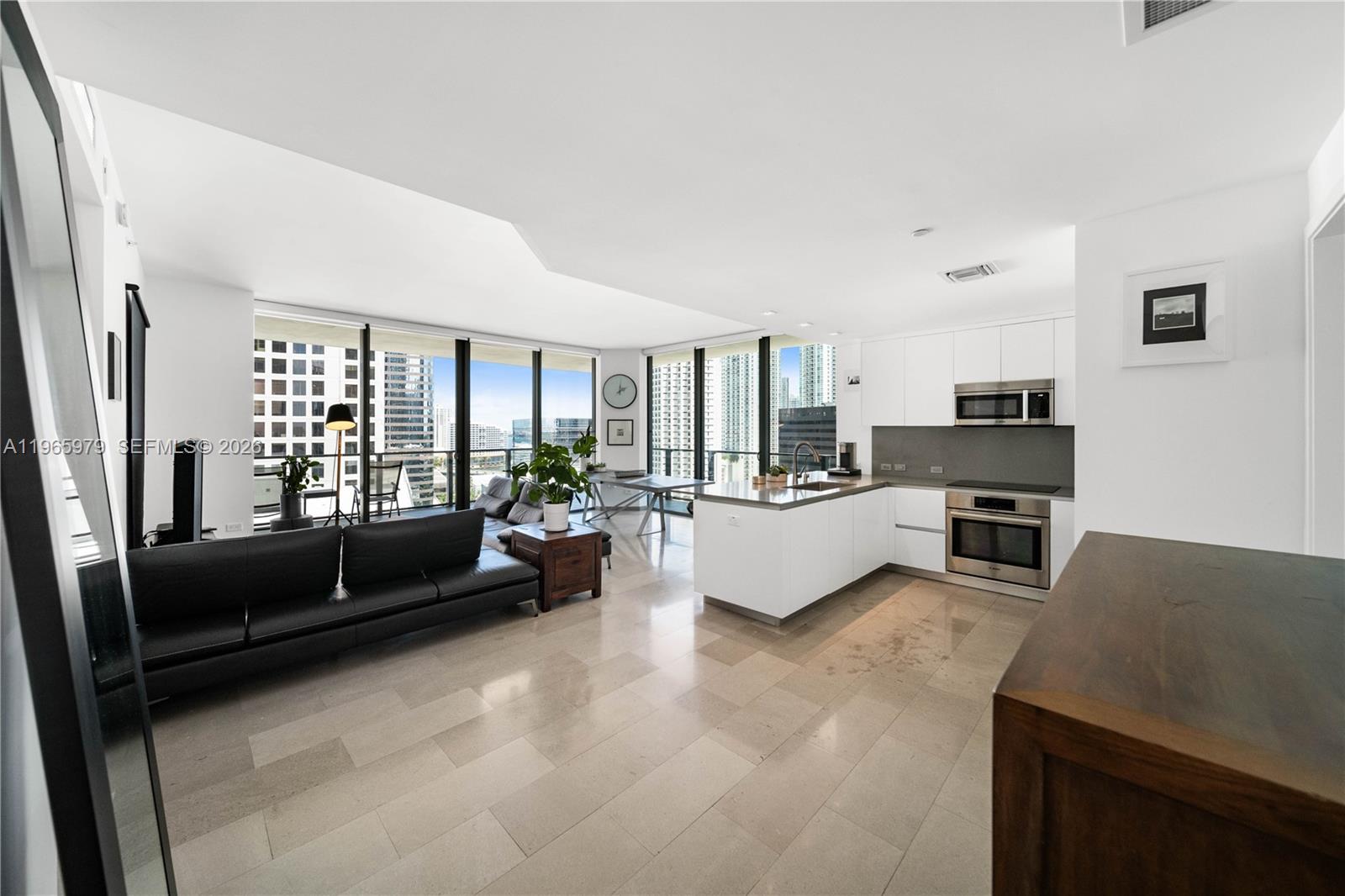 A modern open-concept living area features a kitchen with white cabinetry and tile flooring — 68 SE 6th St # 1201, Miami FL 33131, MIAMI, FL