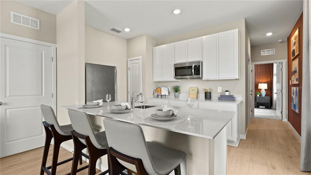 A kitchen features a white island with three chairs, white cabinets, and light wood flooring — 5561 MORANT BAY PATH, KISSIMMEE, FL