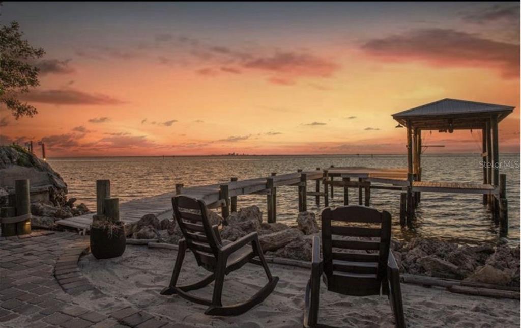 Two rocking chairs sit on a sandy shore overlooking a wooden dock and sunset — 3528 W SHELL POINT ROAD, RUSKIN, FL