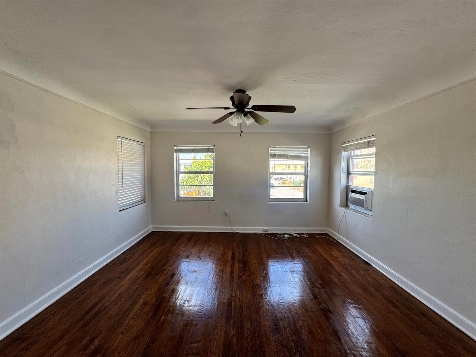 An empty room with dark hardwood floors, a ceiling fan, and four windows — 14 S M Street # 3, FL 33460, FL