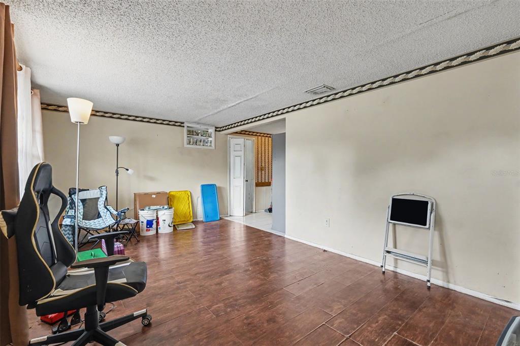 A living room features wood-look tile flooring, beige walls with a decorative border, and a gaming chair — 3317 BAINBRIDGE DRIVE, HOLIDAY, FL