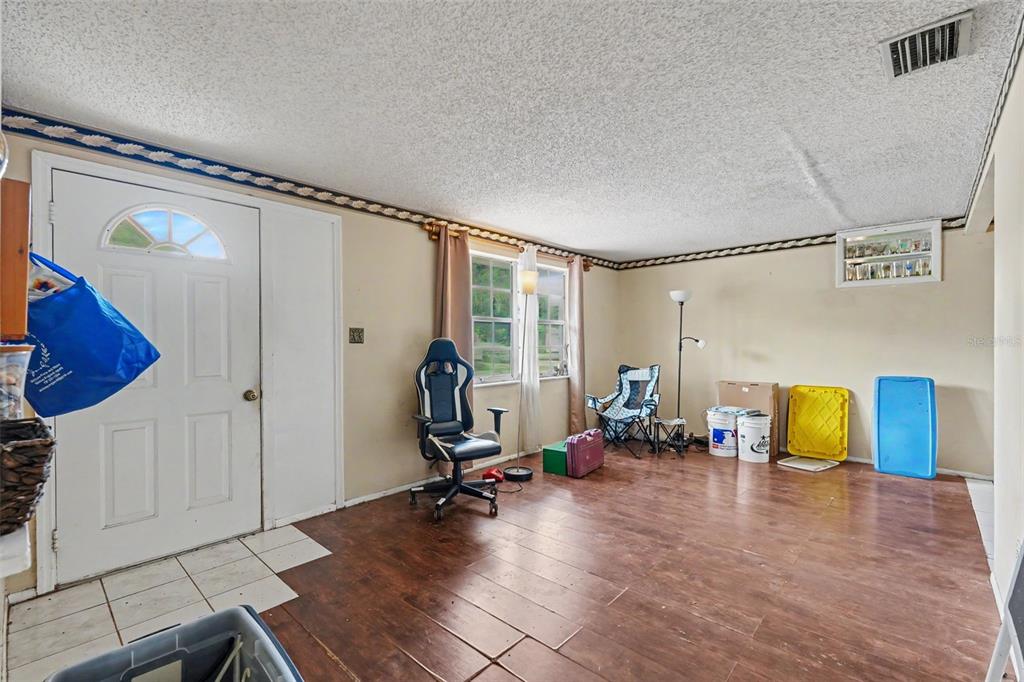 A living room with wood-look flooring, a white front door, and a gaming chair — 3317 BAINBRIDGE DRIVE, HOLIDAY, FL
