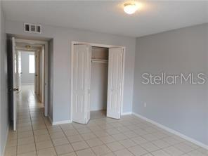 A bedroom with light gray walls, tile flooring, and an open white bi-fold closet door — 2929 W OAK RIDGE ROAD UNIT E8, ORLANDO, FL