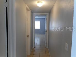 A hallway with light-colored walls and tiled flooring leads to a doorway into another room — 2929 W OAK RIDGE ROAD UNIT E8, ORLANDO, FL