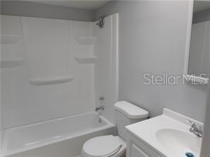 A bathroom features a white vanity, a toilet, and a shower-tub combination with built-in shelves — 2929 W OAK RIDGE ROAD UNIT E8, ORLANDO, FL