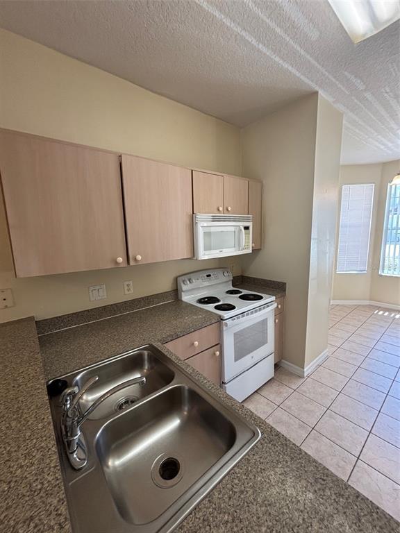 A kitchen features light wood cabinets, a stainless steel sink, and white appliances — 1237 S BEACH CIRCLE, KISSIMMEE, FL
