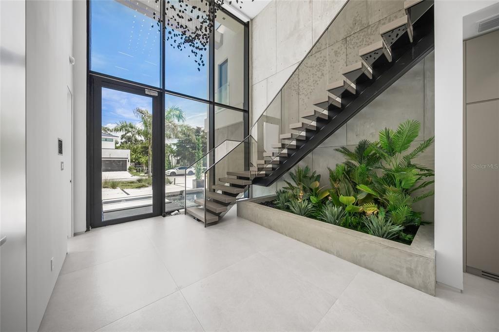 A modern entryway features a floating staircase, floor-to-ceiling windows, and an indoor concrete planter — 1640 WALDEMERE STREET, SARASOTA, FL