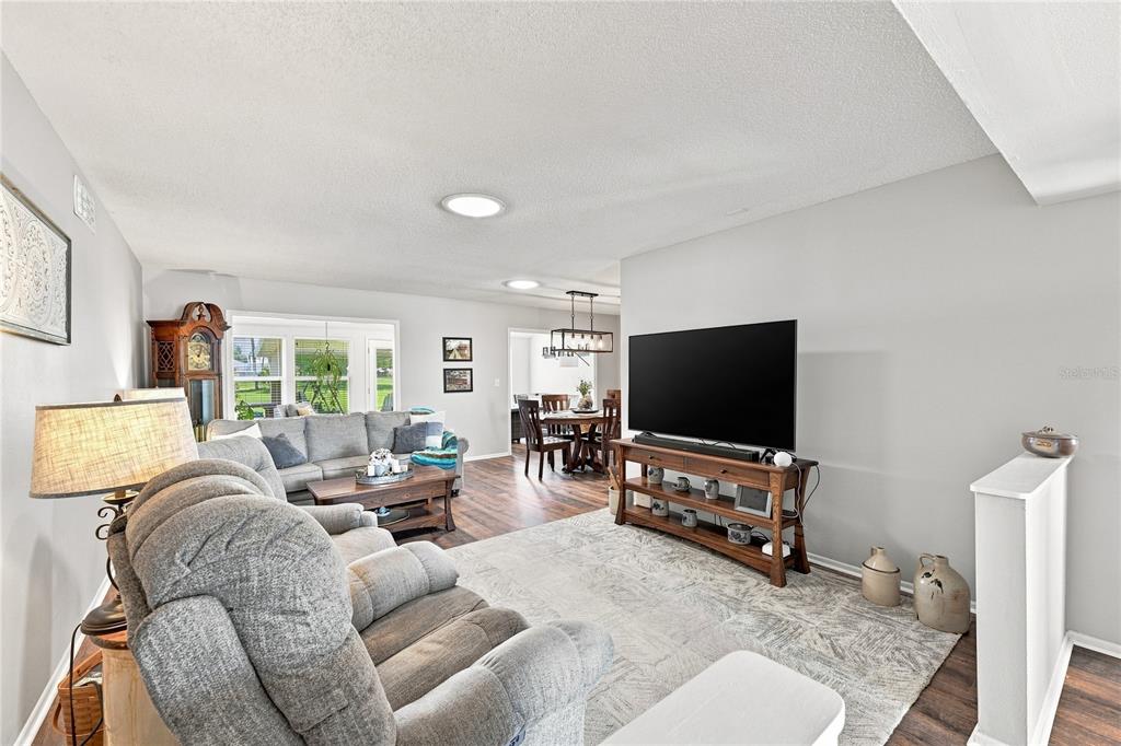 A living room with gray furniture, a television on a wooden stand, and dining area — 1405 HACIENDA DRIVE, SUN CITY CENTER, FL
