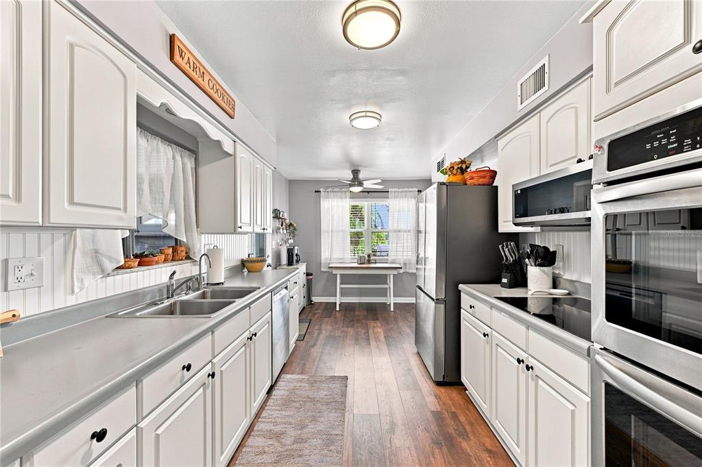 A galley kitchen features white cabinets, stainless steel appliances, and wood-look flooring — 1405 HACIENDA DRIVE, SUN CITY CENTER, FL
